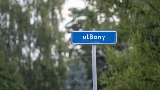 Tabliczka z nazwą ulicy Bony w Ciechanowie na tle drzew.