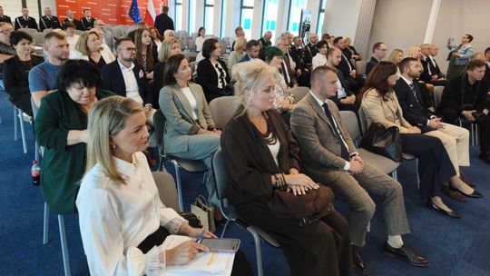 Uczestnicy spotkania siedzą na krzesłach w sali z oznaczeniami samorządu Mazowsza