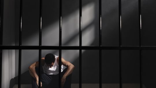 Mężczyzna siedzi na podłodze za krata w areszcie