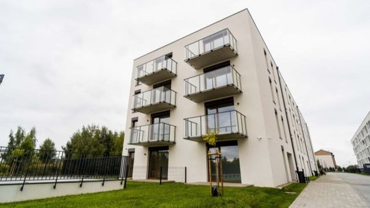 Nowy jasny blok mieszkalny z balkonami ze szklanymi balustradami i chodnikiem w Ciechanowie