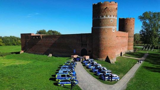 Radiowozy i policjanci ustawieni przed Zamkiem Książąt Mazowieckich w Ciechanowie, widok z góry.