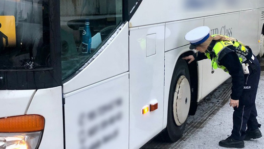 Policjantka w mundurze stoi obok autokaru podczas zimowej kontroli drogowej.