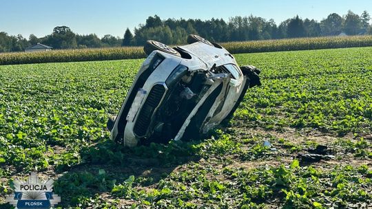 Uszkodzona biała skoda przewrócona na polu, z zamazaną tablicą rejestracyjną