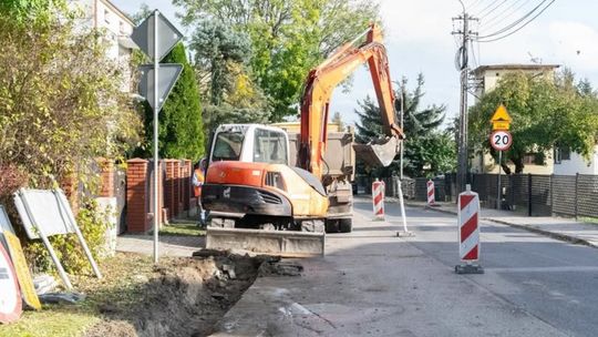 Koparka przy wykopie wzdłuż ulicy Bony w Ciechanowie, obok oznakowanie robót drogowych.