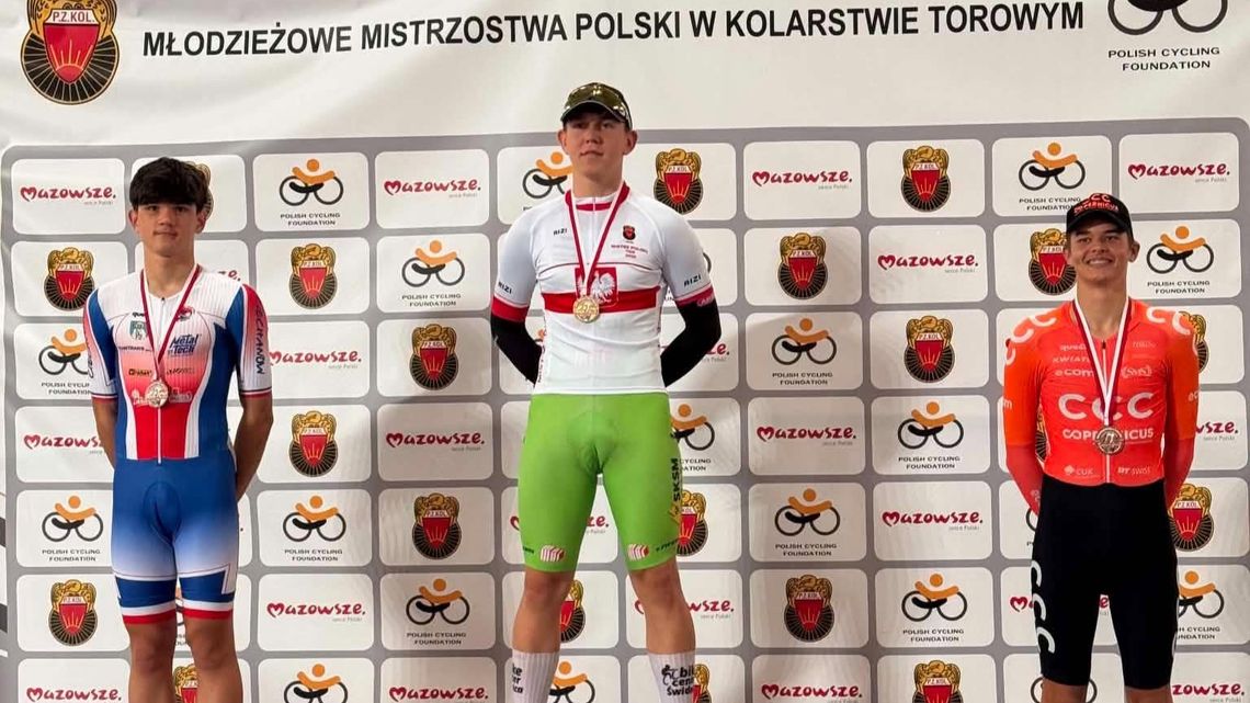 Trzech kolarzy z medalami stoi przed ścianką młodzieżowych mistrzostw Polski w kolarstwie torowym.
