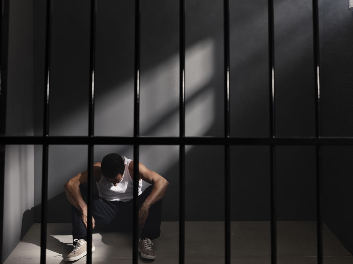 Mężczyzna siedzi na podłodze za krata w areszcie